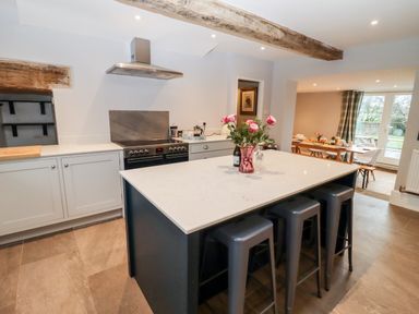 A kitchen with an island and stools a stove and hood with flowers on the island at Ley Mill Farm in Huntley
