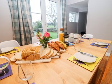 A dining table set with bread croissants bananas orange juice coffee cups and place settings in a room with windows and plaid curtains at Ley Mill Farm in Huntley
