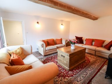 A living room with three sofas a wooden coffee table with flowers and a patterned rug at Ley Mill Farm in Huntley