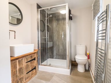A bathroom with a shower enclosure toilet sink with wooden cabinet and chrome towel rail at Ley Mill Farm in Huntley