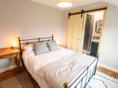 A bedroom with a bed and two pillows next to a wooden table and a sliding door leading to a bathroom at Ley Mill Farm in Huntley