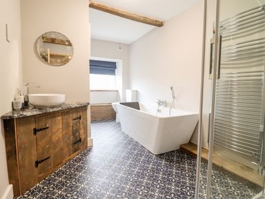 A bathroom with a freestanding bathtub a wooden vanity with a sink a patterned tile floor and a round mirror at Ley Mill Farm in Huntley