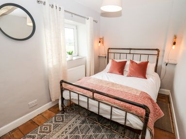 A bedroom with a metal bed frame white bedding and pink pillows a window with curtains and a small plant on the sill at Ley Mill Farm in Huntley