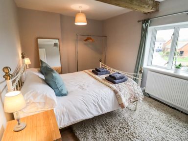 A bedroom with a bed with folded towels and pillows a wooden nightstand with a lamp a floor mirror a window with curtains and a rug at Ley Mill Farm in Huntley