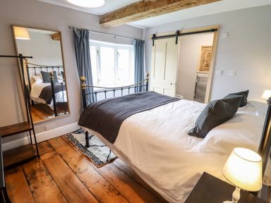 A bedroom with a black metal bed frame white bedding blue pillows wooden floor a mirror and a sliding door at Ley Mill Farm in Huntley