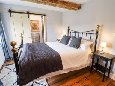 A bedroom with a metal bed frame two pillows bedside tables with lamps wooden floor and a sliding door at Ley Mill Farm in Huntley