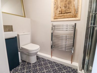 A bathroom with a toilet a small sink a chrome towel rack patterned floor tiles and a wooden wall cabinet at Ley Mill Farm in Huntley