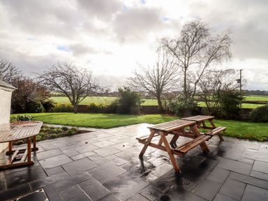 An outdoor patio with wooden picnic tables next to a grassy garden with trees and bushes at Ley Mill Farm in Huntley