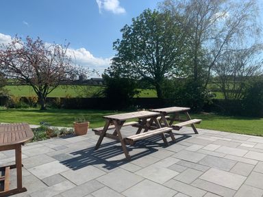 An outdoor patio with wooden picnic tables and a garden with trees and grass at Ley Mill Farm in Huntley