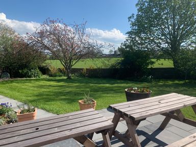 A backyard with green grass, trees, flower pots, and wooden picnic tables at Ley Mill Farm in Huntley
