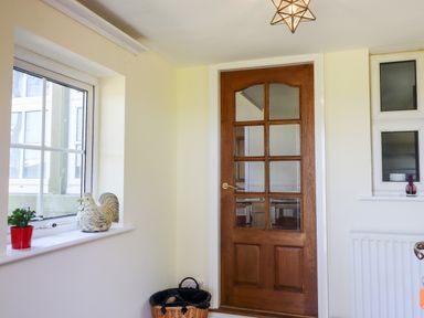 A wooden door with glass panels next to a window with a plant and a decorative rooster on the sill at Buzzards Rest in Stannington near Morpeth