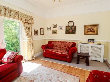 A living room with red sofas pictures on the walls and a door with curtains at Buzzards Rest in Stannington near Morpeth