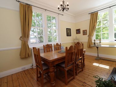 A dining room with a wooden table and six chairs with yellow curtains and windows at Buzzards Rest in Stannington near Morpeth
