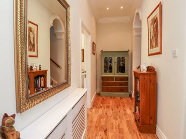 A hallway with wooden floor a green cabinet a tall wooden bookshelf a large mirror and horse paintings at Buzzards Rest in Stannington near Morpeth