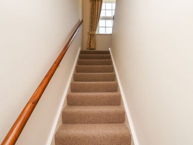 A carpeted staircase with wooden handrail leading to a window with floral curtains at Buzzards Rest in Stannington near Morpeth