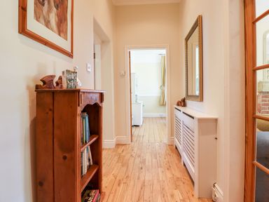 A hallway with wooden floor a small wooden bookshelf and a white radiator cover with a mirror above at Buzzards Rest in Stannington near Morpeth