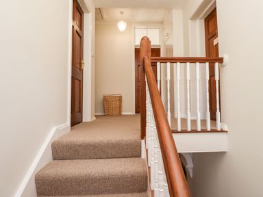 A carpeted staircase leading to a hallway with wooden doors and a wicker basket at Buzzards Rest in Stannington near Morpeth