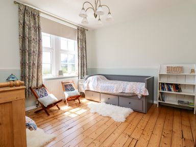 A bedroom with a grey daybed a white bookshelf two wooden chairs and patterned curtains at Buzzards Rest in Stannington near Morpeth