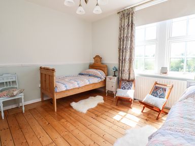 A bedroom with wooden beds two chairs a window with patterned curtains and wooden floor at Buzzards Rest in Stannington near Morpeth