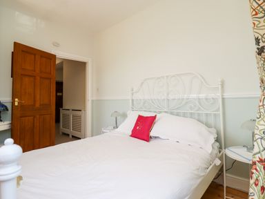 A bedroom with a white metal bed frame a red pillow on the bed bedside tables with lamps and an open wooden door at Buzzards Rest in Stannington near Morpeth