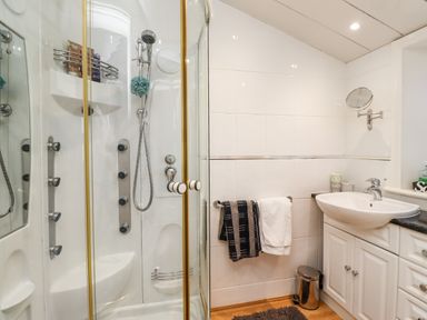 A bathroom with a shower enclosure a sink with cabinets towels on a rail and a small trash bin at Buzzards Rest in Stannington near Morpeth