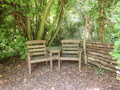 Two wooden chairs connected by a small wooden table in a leafy garden area at Buzzards Rest in Stannington near Morpeth