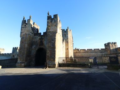 An entrance gate of a stone castle with towers and statues on top under a clear blue sky at Buzzards Rest in Stannington near Morpeth