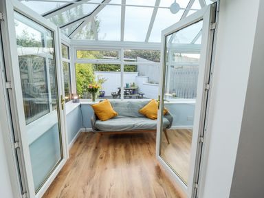 A conservatory with a two-seater sofa with yellow cushions and flowers on the windowsill at Pond Farm View in Hinderwell