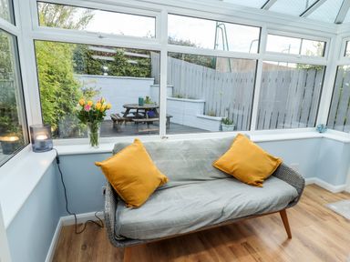 A conservatory with a grey sofa with yellow cushions a lamp and flowers on the windowsill at Pond Farm View in Hinderwell