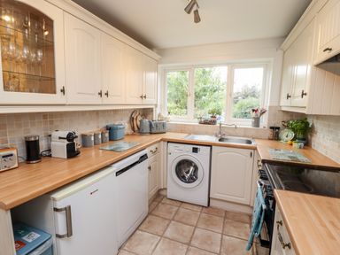 A kitchen with white cabinets wooden countertops a washing machine dishwasher and window at Pond Farm View in Hinderwell