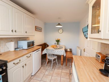A kitchen with wooden counters a dining table with chairs and benches and a wall clock at Pond Farm View in Hinderwell