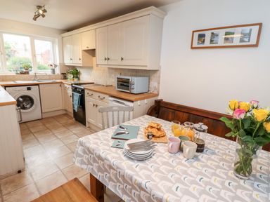 A kitchen with cabinets a washing machine a toaster oven and a table set for breakfast with croissants mugs juice and flowers at Pond Farm View in Hinderwell