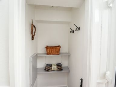 A small storage closet with two shelves holding a wicker basket and a folded wool rug at Pond Farm View in Hinderwell