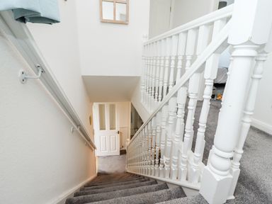 A stairway with white wooden railings and grey carpet leading down to a white door at Pond Farm View in Hinderwell