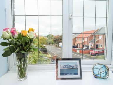 A window with a vase of flowers a framed Staithes picture and a decorative glass float at Pond Farm View in Hinderwell