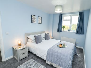 A bedroom with a double bed, bedside tables with lamps, framed pictures on the wall and a window with curtains at Pond Farm View in Hinderwell