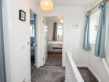 A hallway with gray carpet two doorways leading to bedrooms a window with blue curtains and a white banister at Pond Farm View in Hinderwell