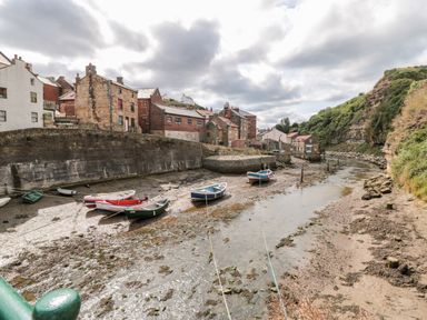 A small harbor with boats pulled up on mud and stone buildings along the water at Pond Farm View in Hinderwell