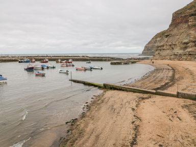 A small harbor with boats moored in calm water next to a sandy beach and cliffs at Pond Farm View in Hinderwell