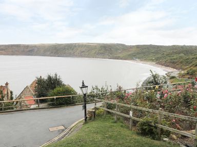 A coastal view with a road, flowers, houses, and a beach surrounded by cliffs at Pond Farm View in Hinderwell