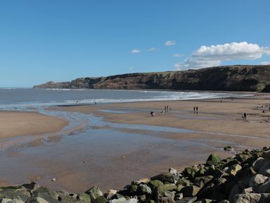 A sandy beach with people walking and cliffs in the background at Pond Farm View in Hinderwell