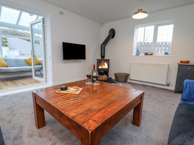 A living room with a wooden coffee table a wood stove a wall mounted tv and an open door to a sunroom at Pond Farm View in Hinderwell