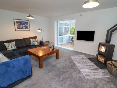 A living room with a sectional sofa a wooden coffee table a wood stove and a wall-mounted television at Pond Farm View in Hinderwell