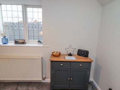 A room corner with a window above a radiator and a small cabinet with decorative items including a star-shaped light at Pond Farm View in Hinderwell