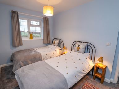 A bedroom with two single beds with bee themed bedding and a window with curtains at Pond Farm View in Hinderwell