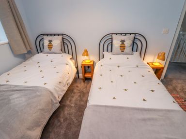 A bedroom with two single beds with bee-themed bedding and pillows with bedside tables and lamps at Pond Farm View in Hinderwell