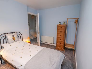A bedroom with a single bed with bee-themed bedding a wooden chest of drawers a wooden clothing rack and a door open to a hallway at Pond Farm View in Hinderwell
