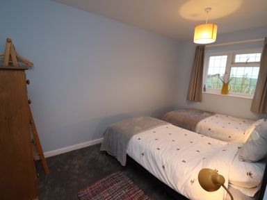 A bedroom with two single beds a wooden dresser a lamp and a window with curtains at Pond Farm View in Hinderwell