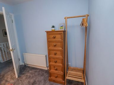 A blue room with a wooden chest of drawers and a wooden clothes rack with hangers at Pond Farm View in Hinderwell