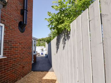A narrow outdoor pathway with a brick wall on the left and a white wooden fence on the right at Pond Farm View in Hinderwell
